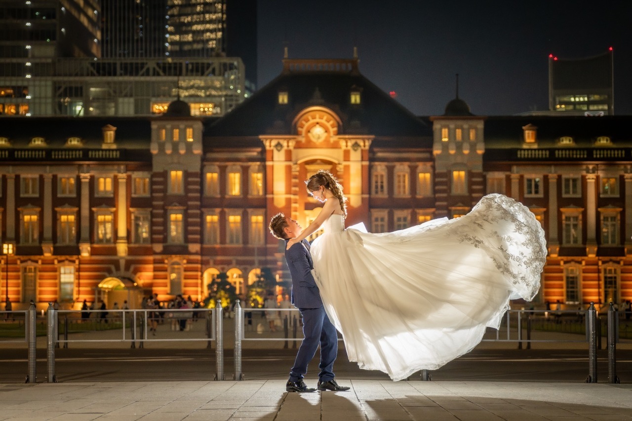 ライトアップされた東京駅を背景に新婦を抱き上げ、白いドレスを大きく広げた前撮り写真