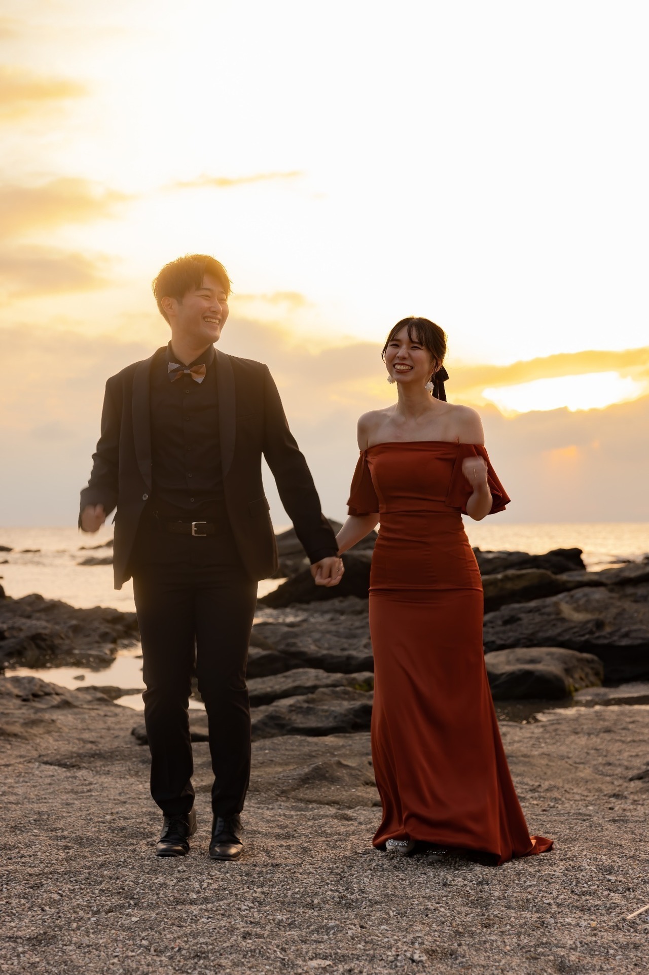 城ヶ島の夕陽を背景に手をつないで歩くオレンジドレスの新郎新婦