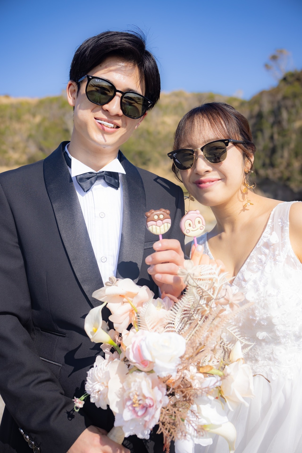 青空の城ヶ島でサングラスをかけキャラクタースイーツを持つ新郎新婦