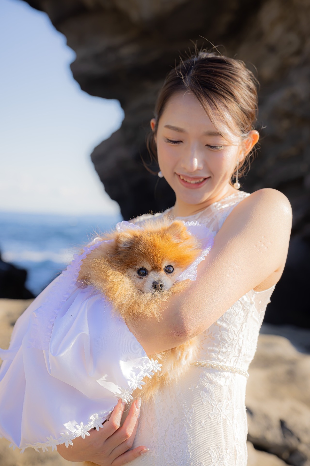城ヶ島の海辺でウェディングドレス姿の新婦が愛犬を優しく抱く前撮り写真