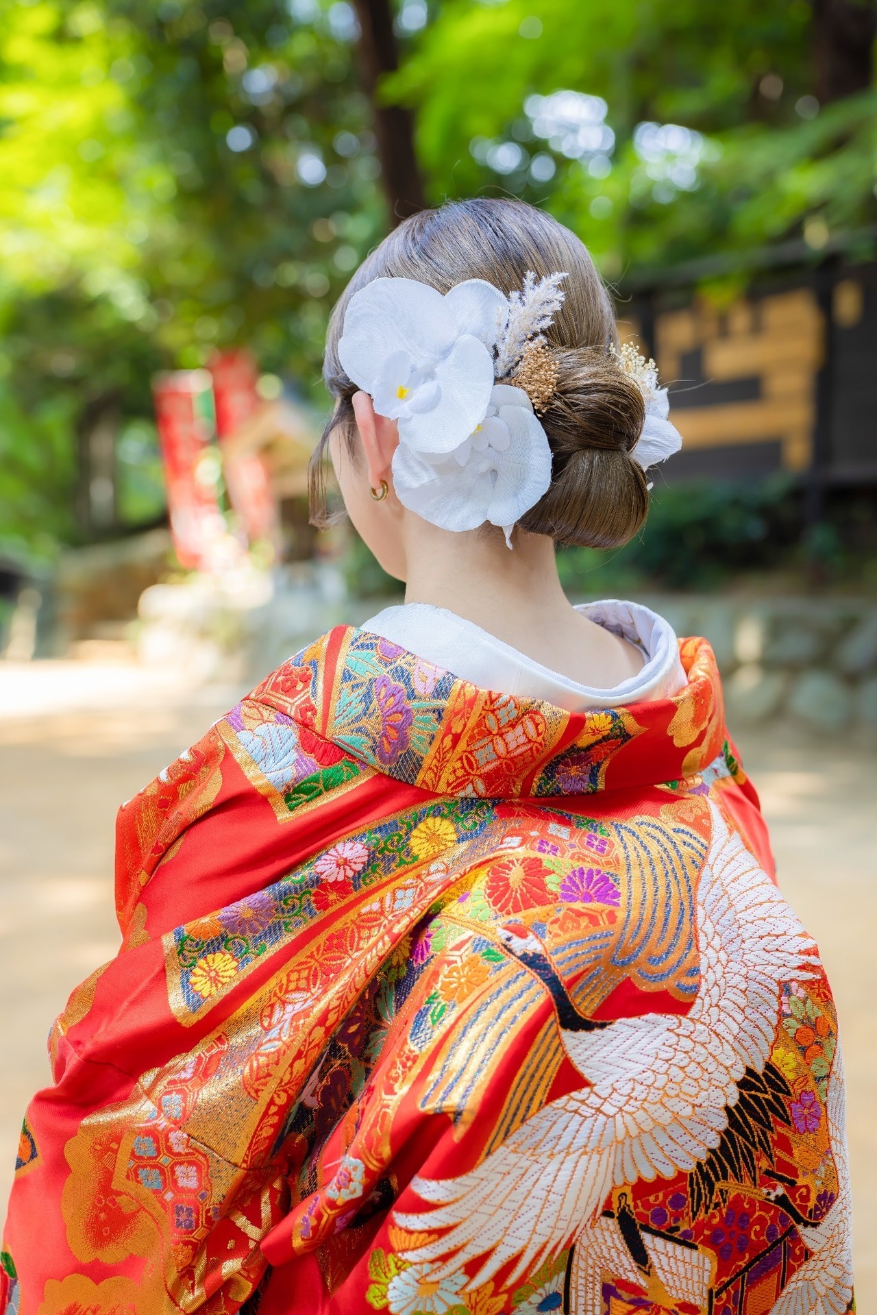 鮮やかな赤い色打掛と白い胡蝶蘭の髪飾りを写した新婦の後ろ姿