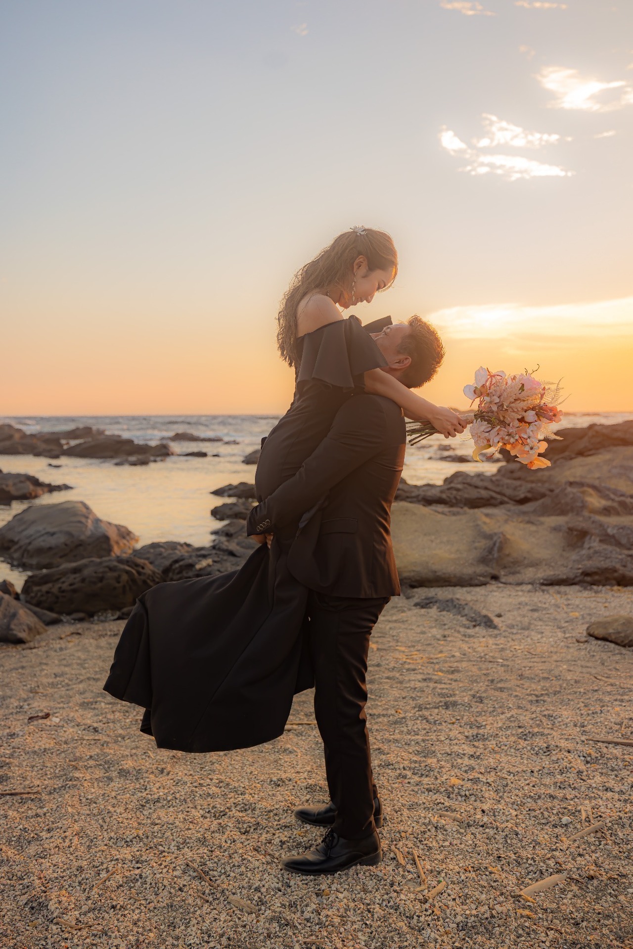 夕暮れの城ヶ島の海辺でブラックドレスの新婦を抱き上げる新郎