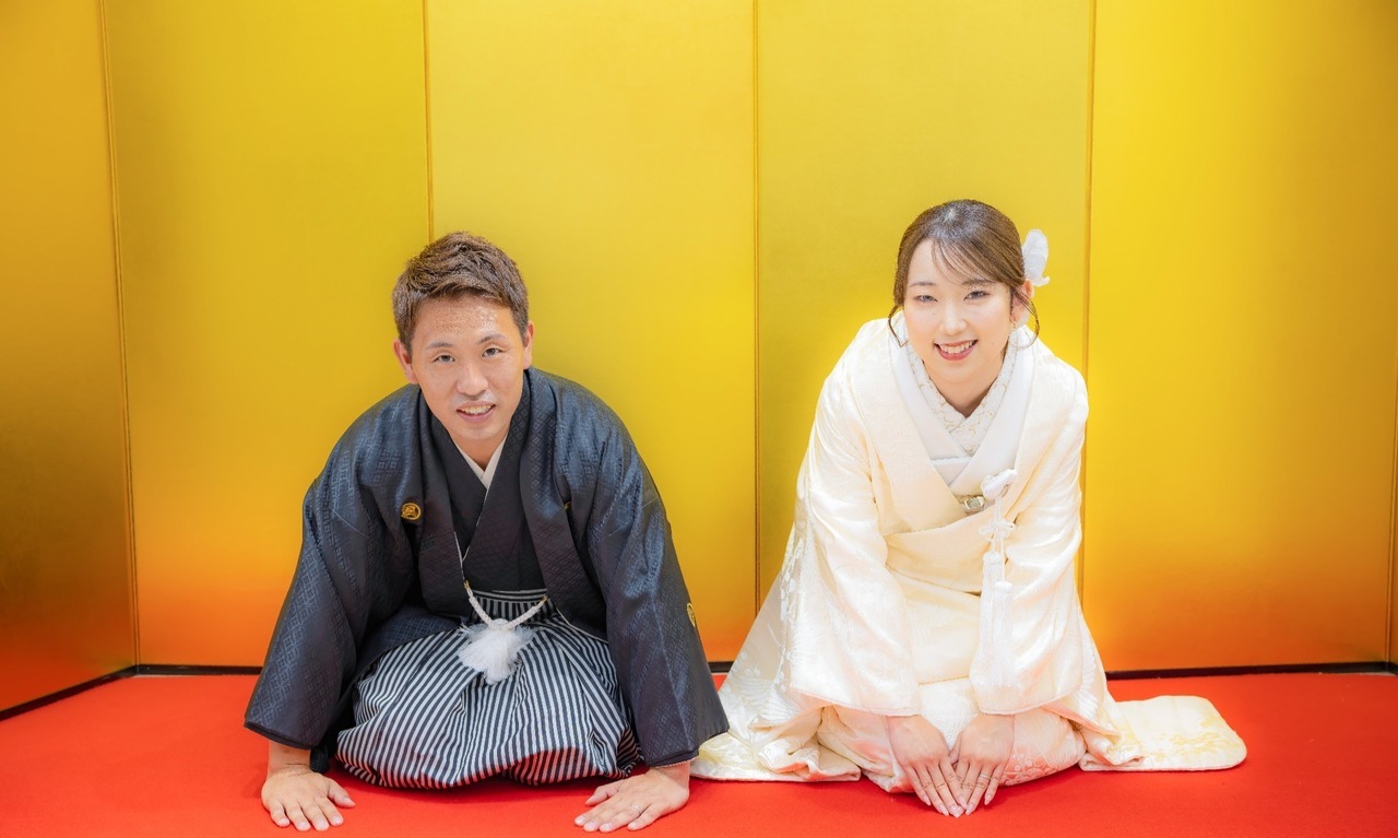金屏風の前で白無垢と黒紋付袴姿で正座する新郎新婦