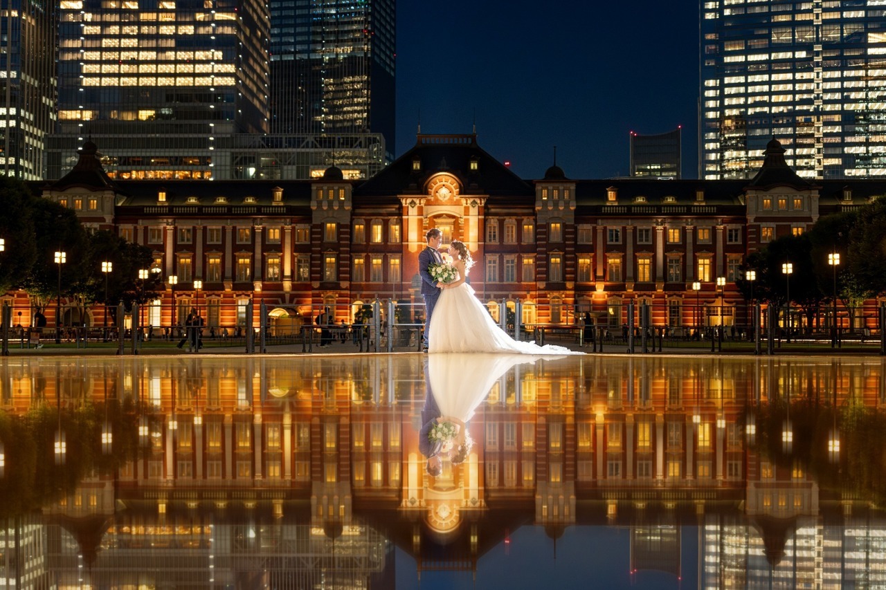 ライトアップされた東京駅と水面のリフレクションを背景に立つ新郎新婦