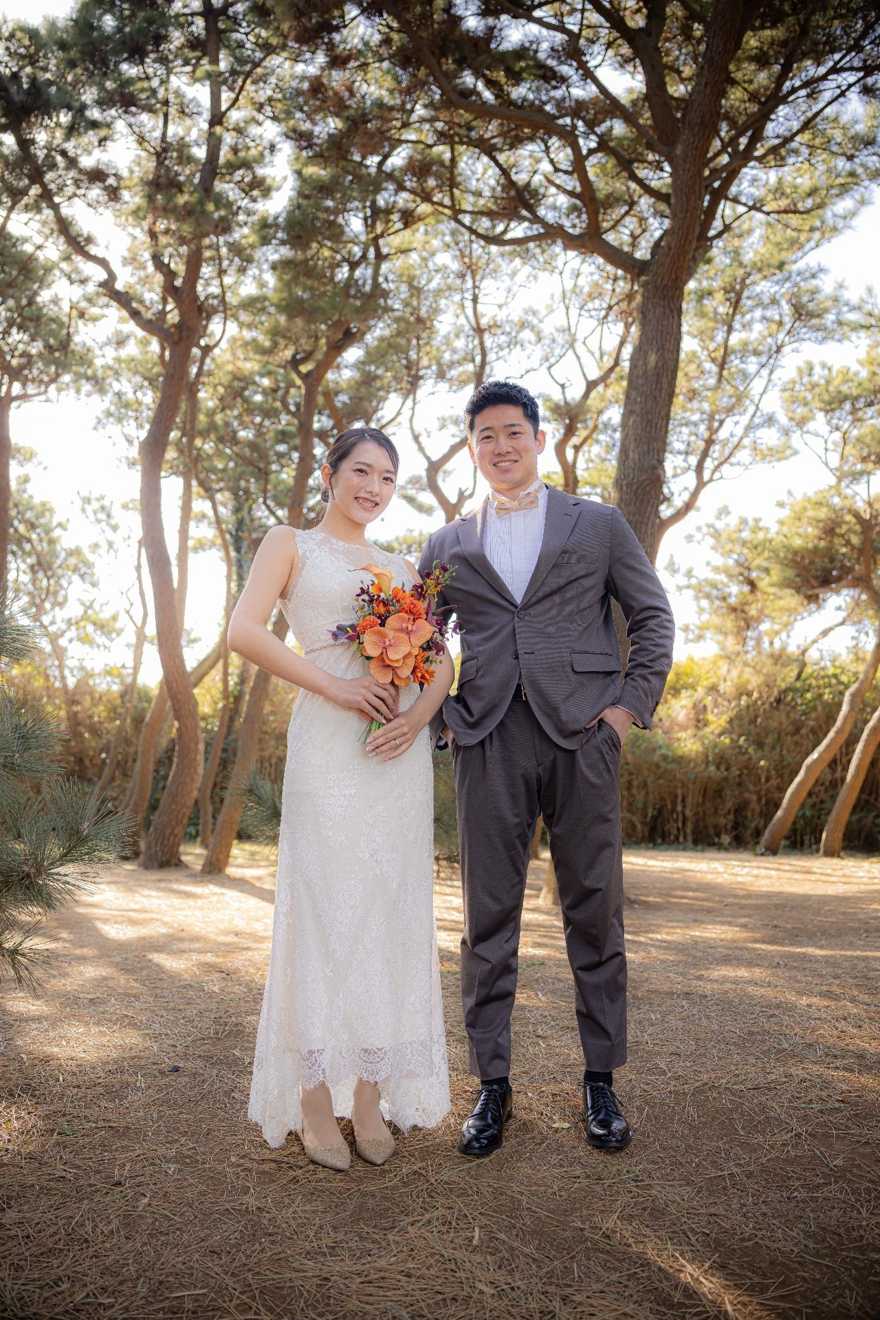 城ヶ島の松林でウェディングドレスとタキシード姿で並ぶ新郎新婦の全身前撮り写真